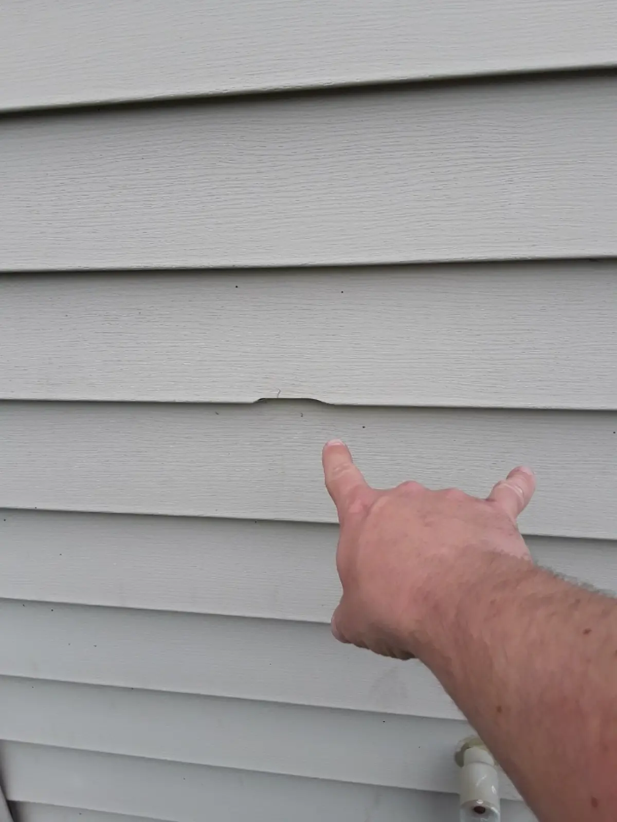 Hail damage crack on vinyl siding shown during a storm damage inspection on a Minnesota home