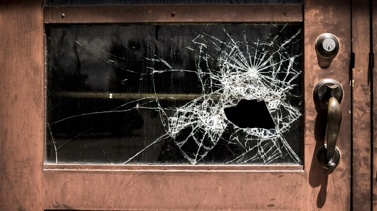 Close-up of hail-damaged window with cracked glass and dented frame on a Minnesota home