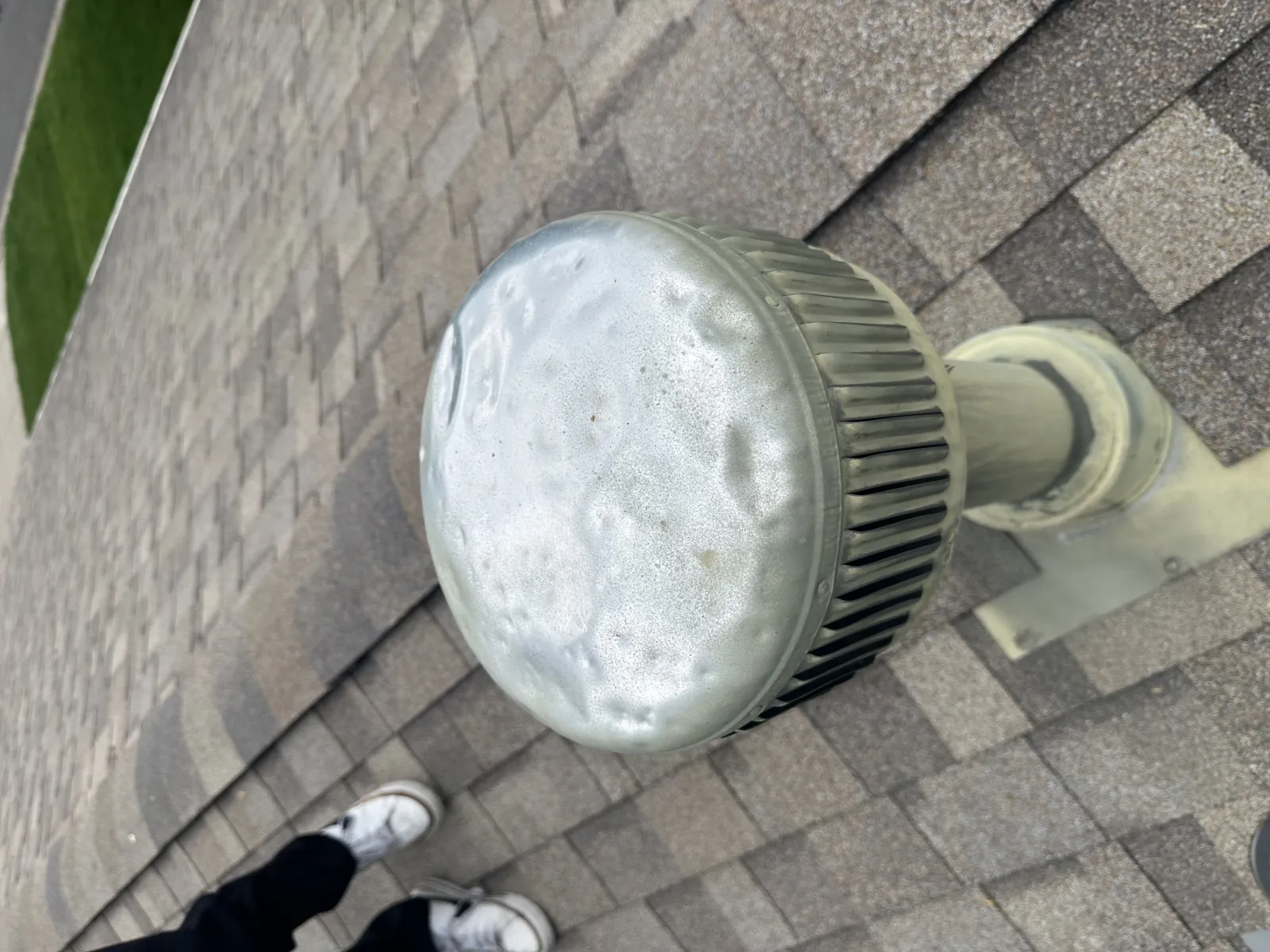 Hail-dented metal roof vent cap showing multiple impact dents from a severe storm on a residential rooftop
